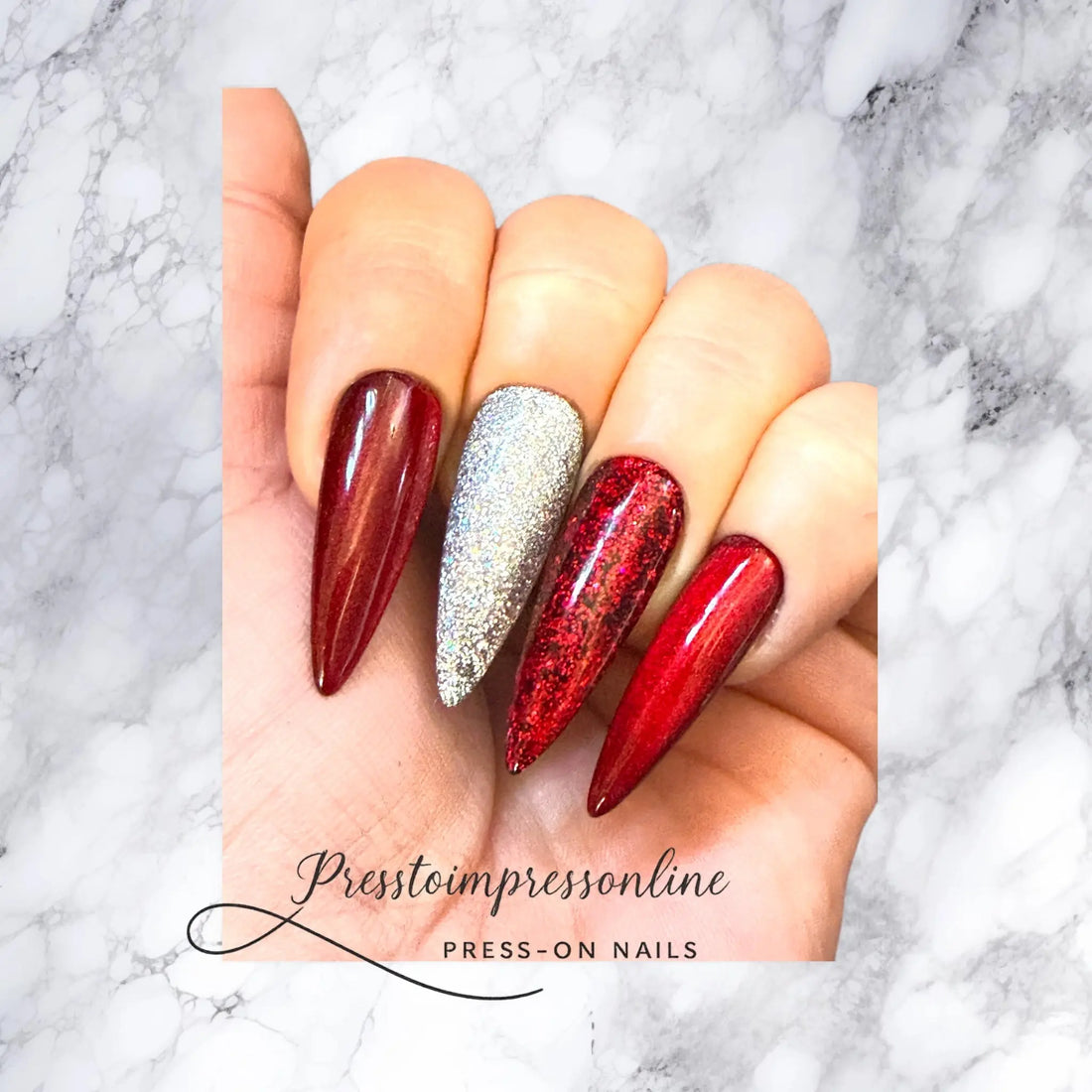 “Hand wearing long red and silver stiletto press-on nails from Presstoimpressonline displayed on a marble background.”