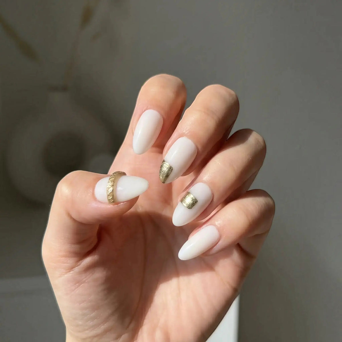 Press to Impress Gold Muse almond-shaped nails with milky white base and gold foil accents. Elegant design for everyday or special occasions.