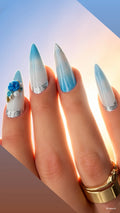 Luxury handmade blue ombré press-on nails with pearlescent shimmer, silver glitter accents, and 3D blue floral embellishments from the Aruba At Sunset Collection.