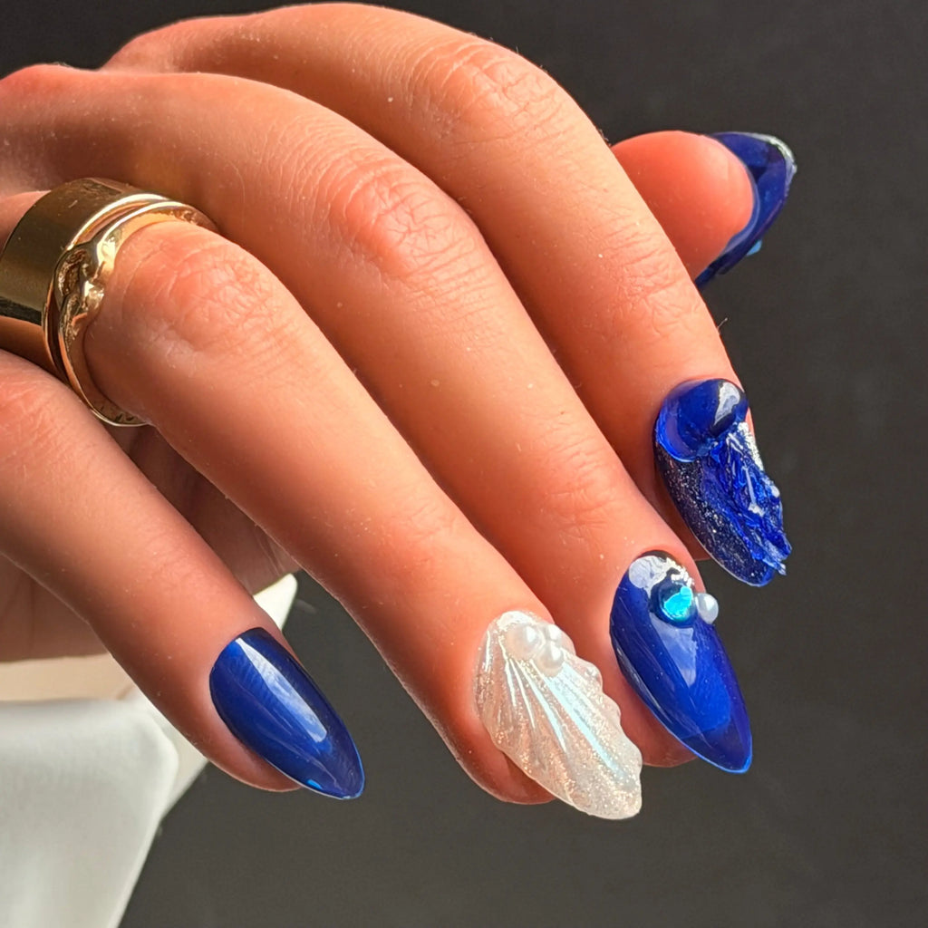 Luxury blue chrome press-on nails featuring 3D shell accents, ocean-inspired textures, and water droplet embellishments.