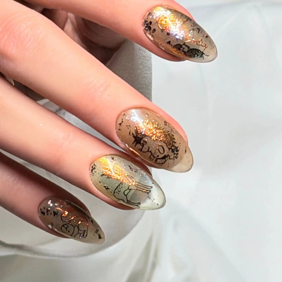 Close-up of Gilded Folklore press-on nail with intricate black vintage-style illustration, gold accents and metallic details