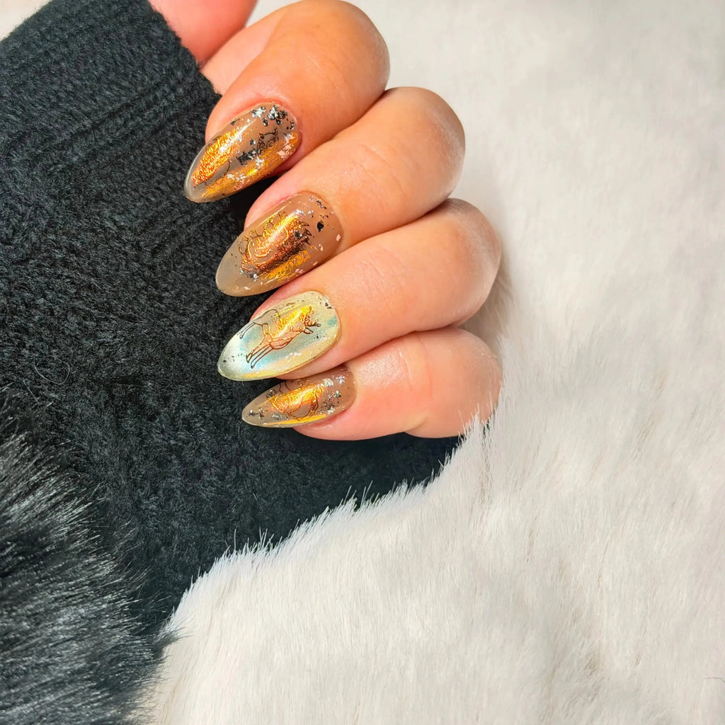 Gilded Folklore handmade press-on nails with sheer neutral base, black illustrated details and luminous gold accents