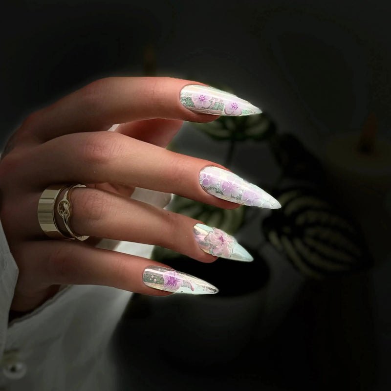 Handmade luxury press-on nails featuring iridescent pearl chrome, soft pink hand-painted blossoms, a 3D flower accent, glossy finish, and long almond-shaped nails.