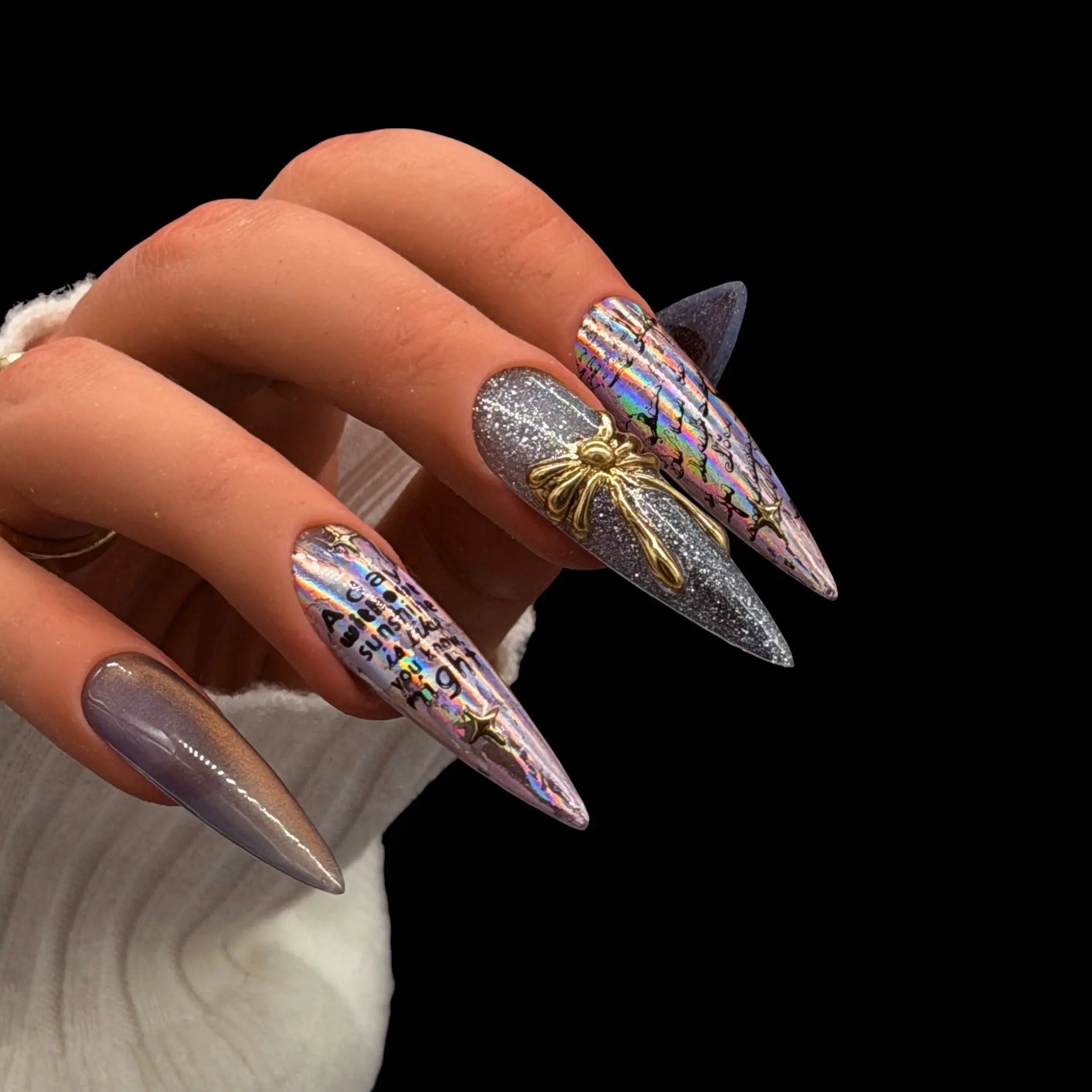 Holographic chrome stiletto press-on nails with silver shimmer, gold accent detail, and iridescent foil design