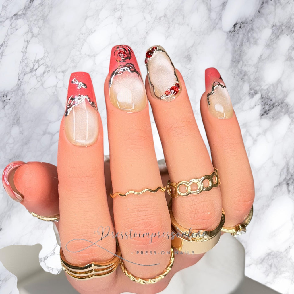 Luxury blush ombré press-on nails with chrome outlines and red crystal accents on square nails