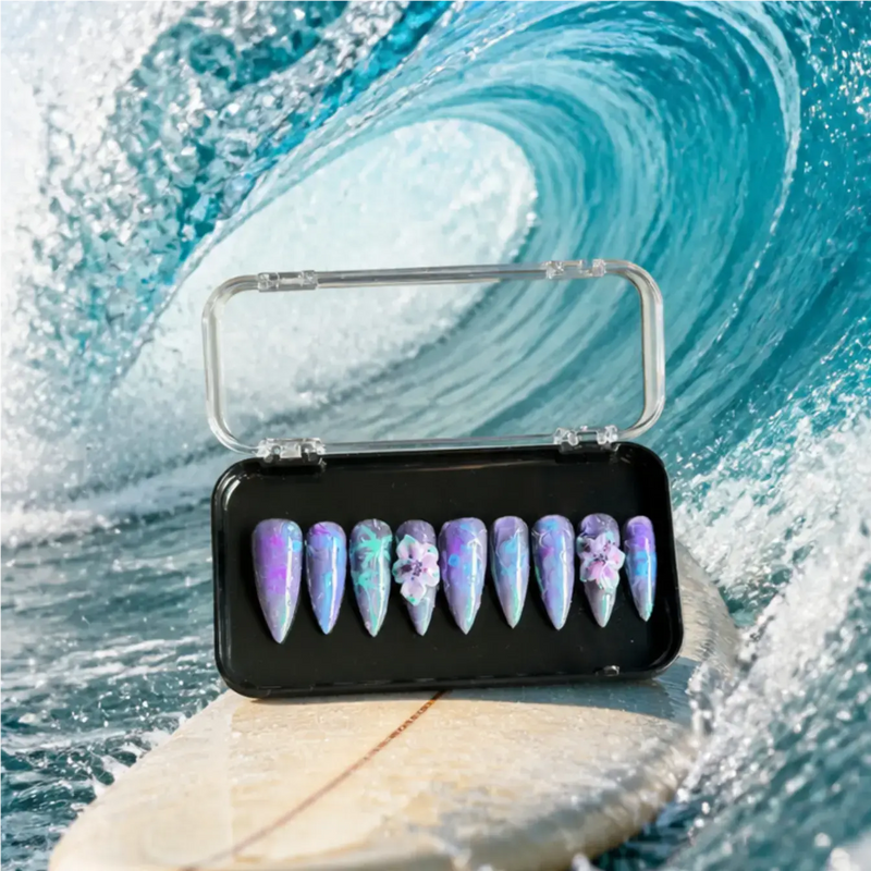 Handmade luxury press-on nails in lavender, purple, and iridescent blue with hand-painted tropical leaves, 3D orchid flowers, chrome shimmer, and a glossy long stiletto shape.