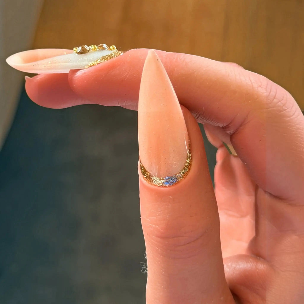 Press to Impress Antigua stiletto press-on nail with champagne shimmer, gold glitter cuticle detail, and embellishment