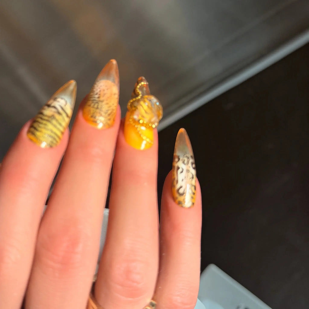 Press to Impress Golden Safari press-on nails with amber glass French tips, animal print, and gold chain accents.