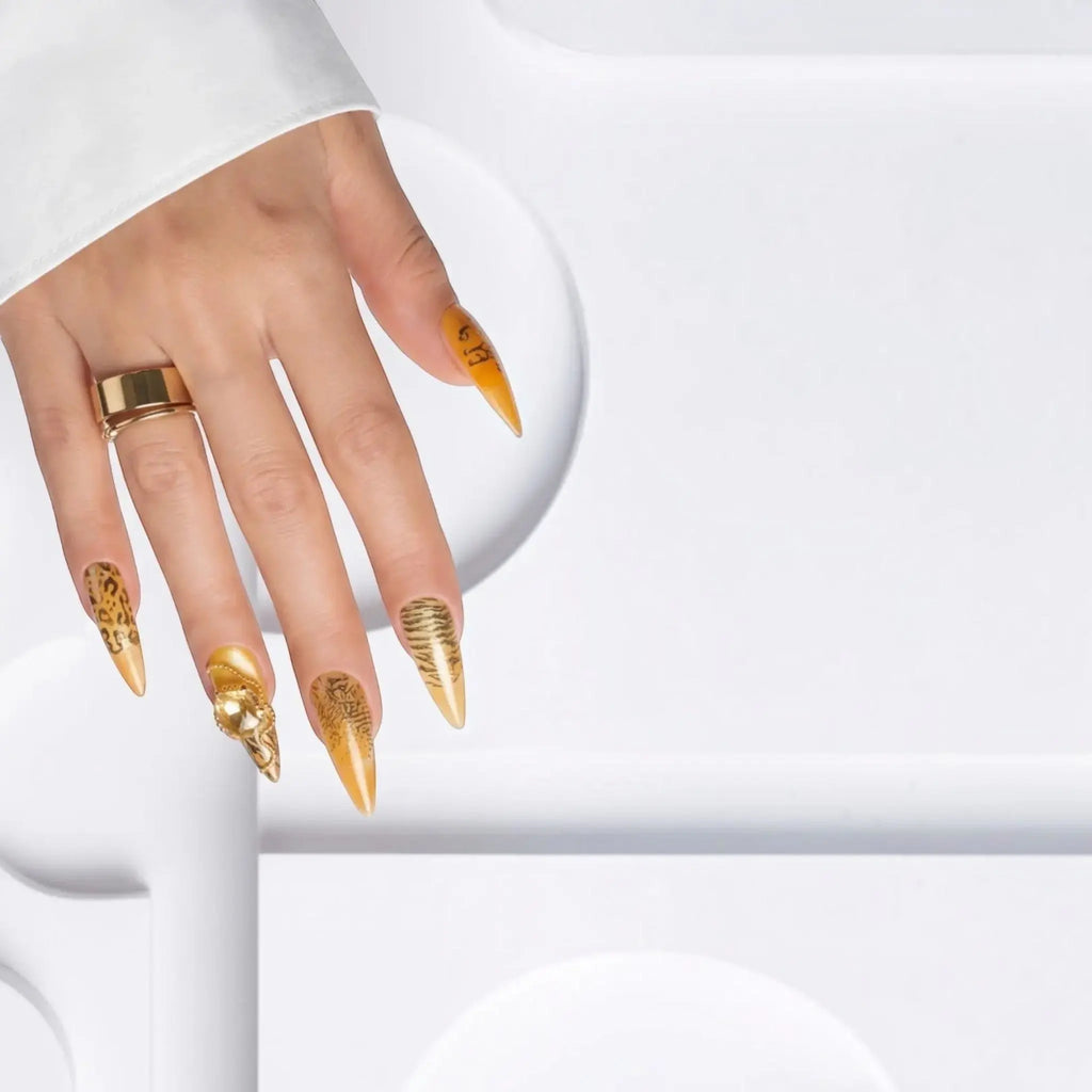 Press to Impress Golden Safari press-on nails with amber French tips, animal print, and gold 3D accents on a hand.