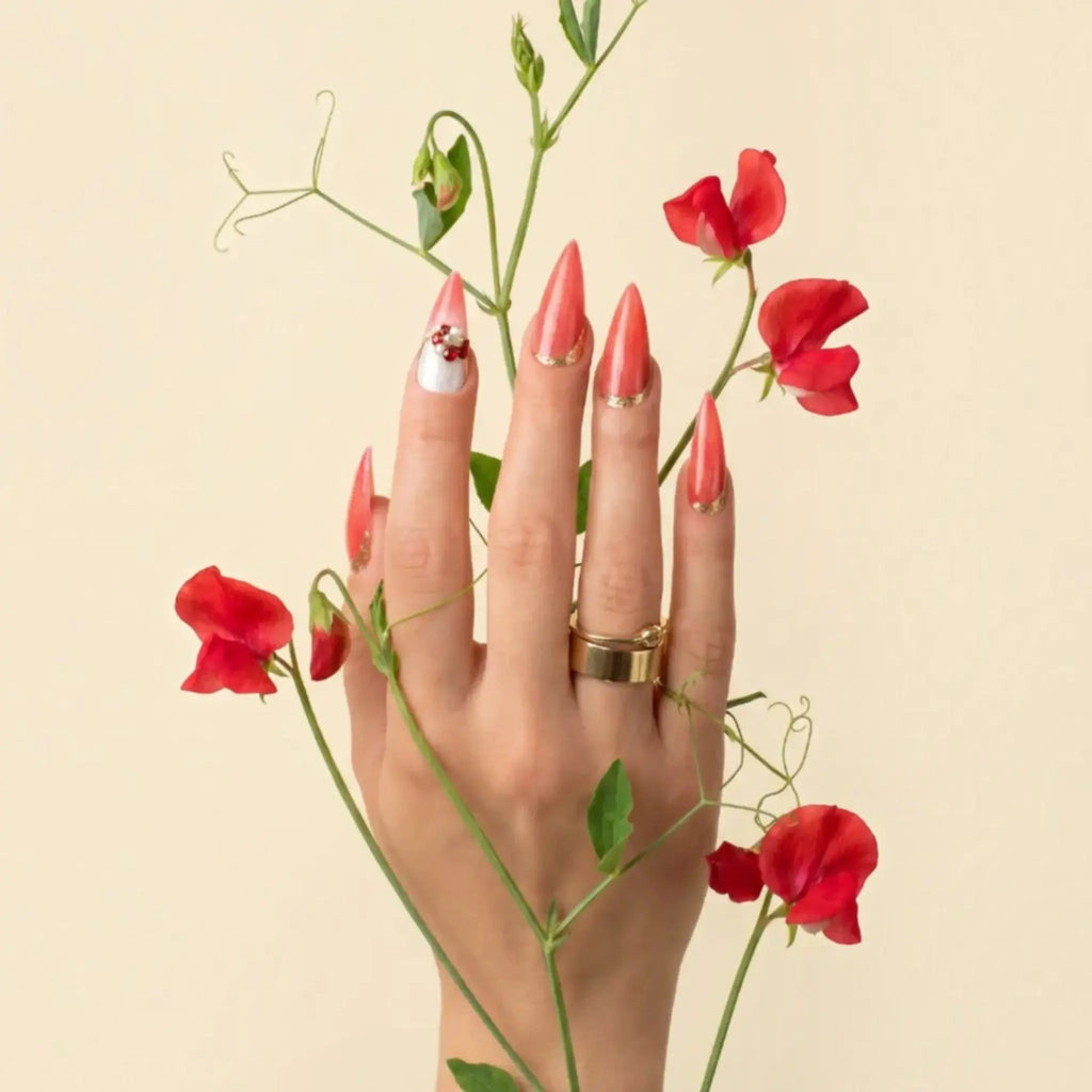 Press to Impress Saint Lucia press-on nails in coral-red with gold accents and crystal embellishments on a hand.