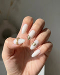 Press to Impress Gold Muse almond-shaped nails with milky white base and gold foil accents. Elegant design for everyday or special occasions.